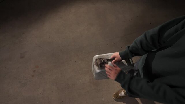 High angle view person walking on a concrete floor while holding a metal jerrycan, symbolizing energy crisis, resource scarcity, and transportation needs in an uncertain economy