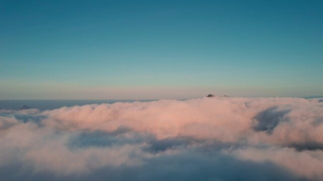 Aerial view of Mount Inerie peak rising above a thick layer of pink-tinted clouds during sunrise in Inerie, East Nusa Tenggara, Indonesia.