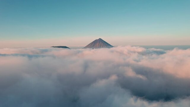 Aerial view of Mount Inerie rising above a thick layer of clouds during golden hour in Inerie, East Nusa Tenggara, Indonesia.