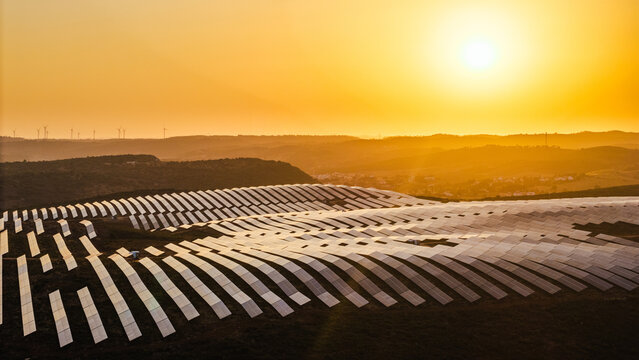 Aerial view of extensive photovoltaic panel arrays glowing in warm evening light across a rural hilly landscape.