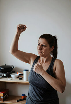 Determined woman in a gray tank top flexing her bicep and making a fist, strength and empowerment