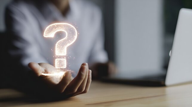 Person holds hand out with a glowing question mark above it near a laptop in a dimly lit room