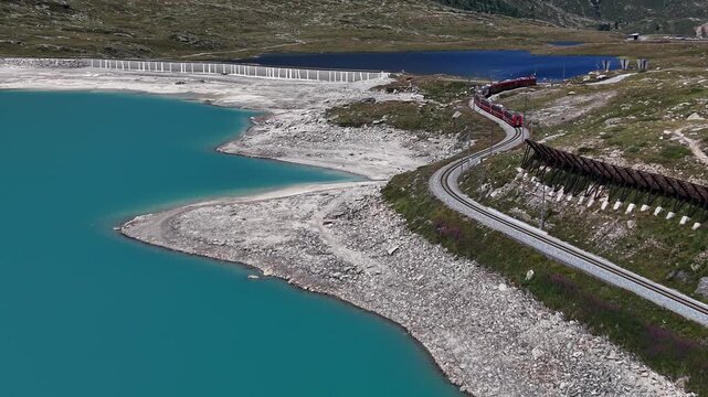 Aerial view of the turquoise waters of Lago Bianco and the Bernina Express train passing along the dam in Poschiavo, Grisons, Switzerland.