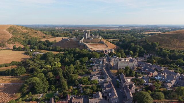 Aerial drone footage of the iconic Corfe Castle in Dorset, England, showcasing the medieval castle ruins, historic village, and rolling Purbeck countryside on a hot summer morning