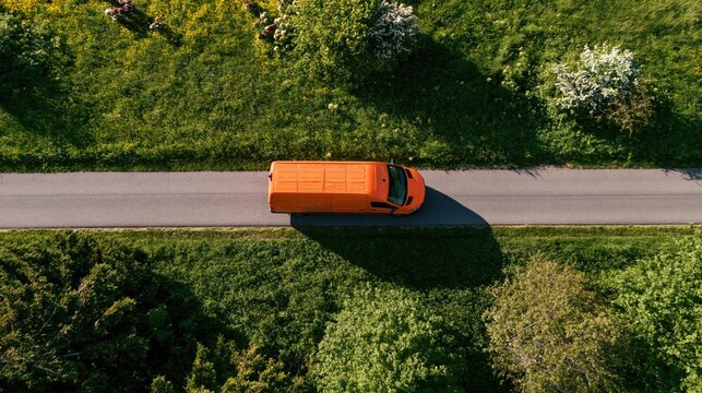 Growth and efficiency shown by an orange van driving on a rural road through green fields and wildflowers in aerial view