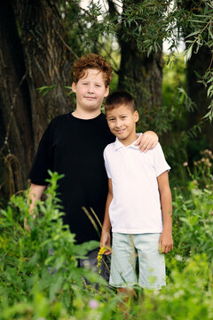 Portrait of two brothers standing together in park greenery during summer day. Concept of siblings bond, brothers relationship, family support, boys childhood, adolescence and growing up.