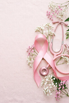 Breast cancer awareness ribbon and pink stethoscope with delicate flowers on soft fabric background