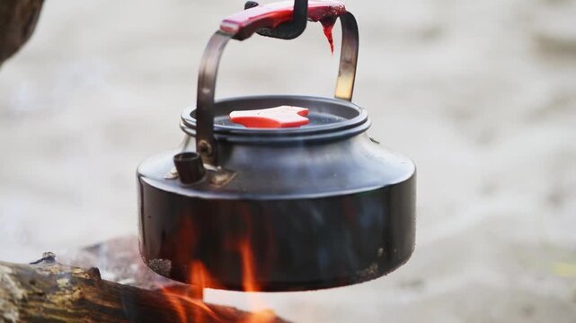 Black kettle heating over bonfire with glowing flames and outdoor background