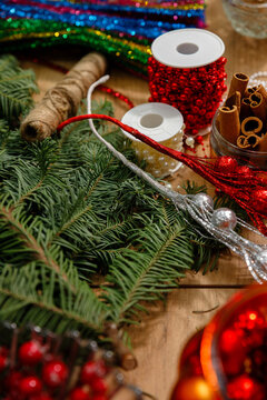 Vertical closeup of christmas crafting materials on wooden table with pine branches glitter ribbons red beads cinnamon sticks and twine for cozy holiday DIY decoration projects