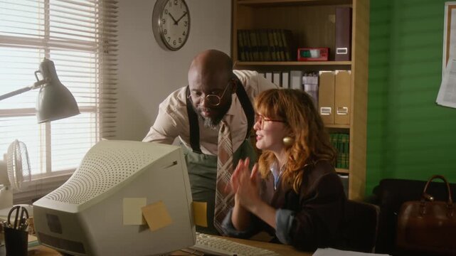 African American man and Caucasian woman discussing data on retro computer in vintage office. Ideal for nostalgic corporate training videos