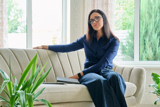 Thoughtful businesswoman leaning on sofa looking at camera during work break at home office
