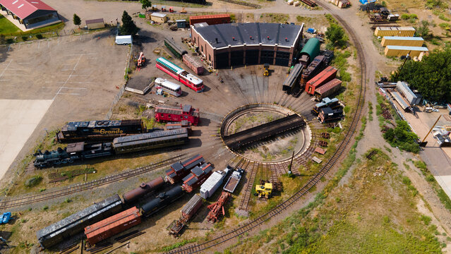 Aerial view of the Colorado Railroad Museum featuring a historic roundhouse, a central turntable, and vintage locomotives and train cars in Golden, Colorado, United States.