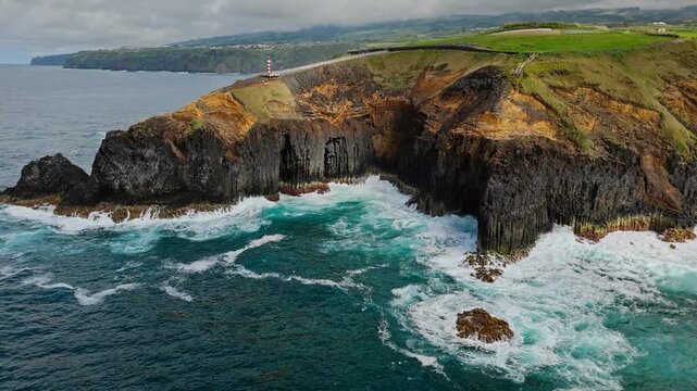 Green volcanic headland bordered by basalt cliffs and foamy Atlantic waves on Sao Miguel island, Azores. Natural island coastline