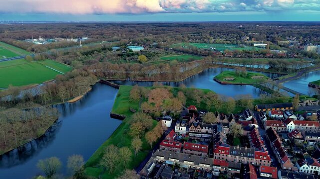 Aerial view video clip of the star fortress bastions and moat canals of Naarden in the Netherlands during sunset with historic houses, green earthen ramparts, and colorful clouds above