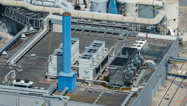 Aerial view of industrial HVAC equipment, cooling towers, and exhaust stacks on the rooftop of a high-tech manufacturing facility in Crolles, Auvergne-Rhone-Alpes, France.