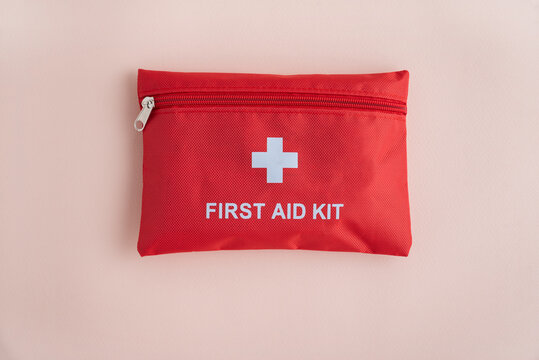 Red first aid kit with white cross and text on a light pink background