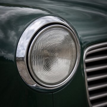 Close-up of a round chrome headlight on a vintage dark green car