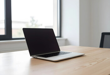 Fototapeta premium Modern silver laptop with a blank dark screen on a light wooden desk in a bright office setting, the setting is a bright office interior with a large window in the background