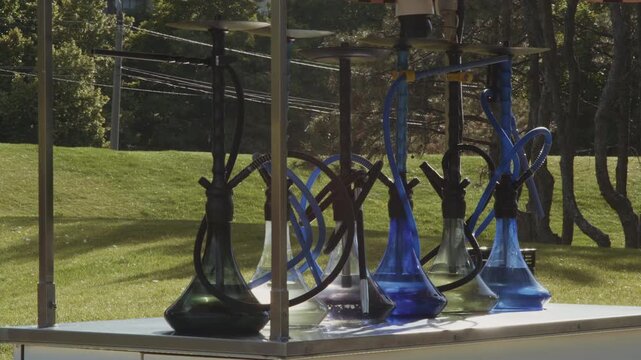 A row of glass hookahs stand on the counter of a street bar in the park