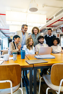Diverse business professionals smiling, actively working together at a long table in a modern coworking office environment, fostering teamwork and partnership