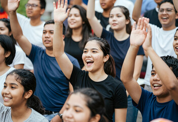Obraz premium Excited young asian woman raising hand in a crowd of diverse people, participation and engagement concept, the group of young adults and teenagers are smiling and cheering
