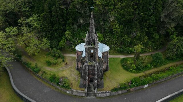 Capela de Nossa Senhora das Vitorias standing by a curved pathway amid lush vegetation in Furnas valley, drone view