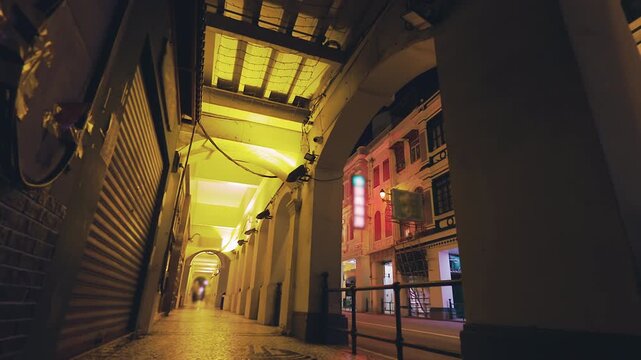 Illuminated historic arched walkway and street at night in Macau