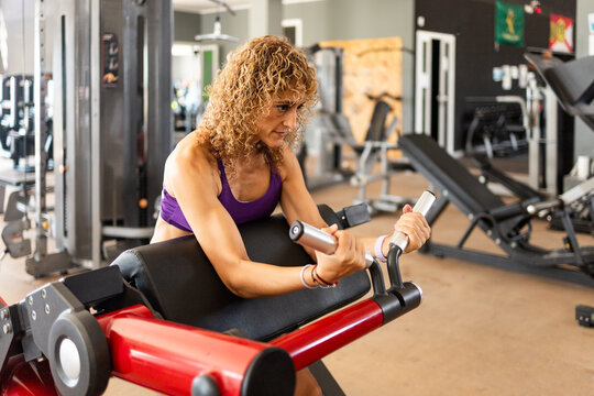 Fit 40-Year-Old Woman Performing a Seated Preacher Curl Exercise on a Strength Machine in a Modern Fitness Gym