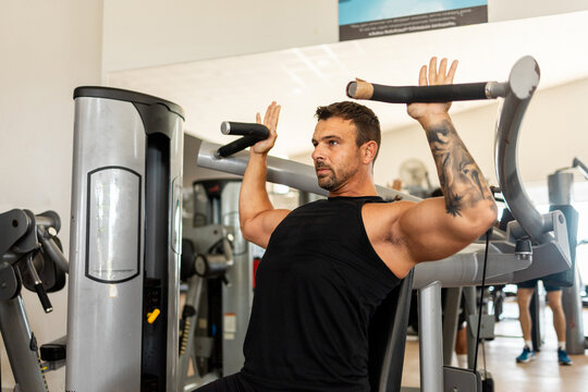 A Muscular 40-Year-Old Man Training His Shoulders on a Seated Shoulder Press Machine in a Modern Gym, Demonstrating Strength, Fitness, and a Healthy Active Lifestyle