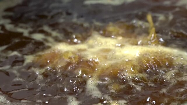 Fresh fish being deep fried in sizzling oil in an iron wok, showcasing traditional cooking.