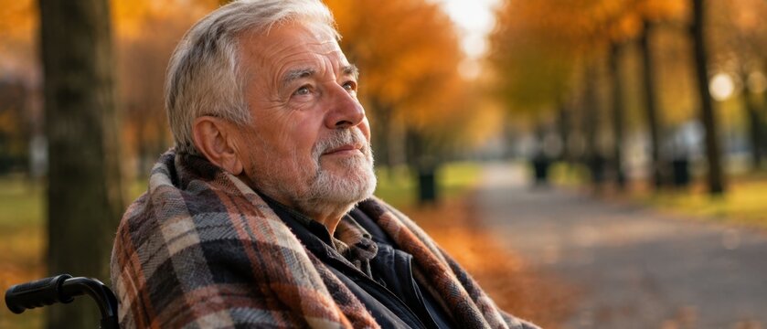 Nachdenklicher &auml;lterer Mann im Rollstuhl mit Karodecke in einem herbstlichen Park. Portr&auml;t eines Seniors im Ruhestand, Konzept f&uuml;r Altenpflege und Weltseniorentag