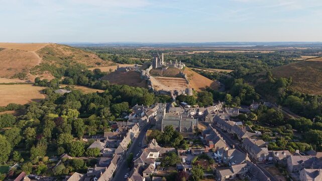 Aerial drone footage of the iconic Corfe Castle in Dorset, England, showcasing the medieval castle ruins, historic village, and rolling Purbeck countryside on a hot summer morning