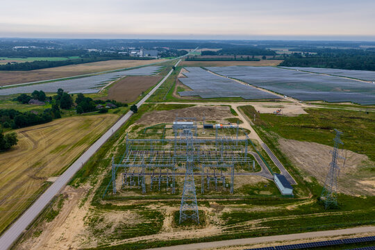 Aerial view of a large solar farm and electrical substation in the countryside, featuring rows of solar panels, power lines, and rural fields in Tume, Tukums Municipality, Latvia.