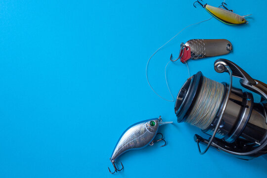 Close‑up of a metallic fishing reel and three colorful lures on a bright blue background. The composition captures craftsmanship, motion, and the spirit of modern angling.