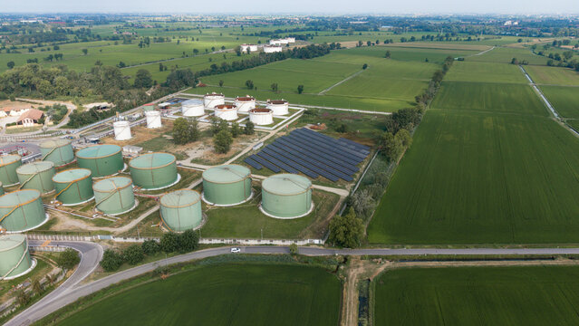 Aerial view of the Sigemi S.r.l. industrial facility featuring large storage tanks, a solar panel array, and surrounding green agricultural fields in Lacchiarella, Lombardia, Italy.