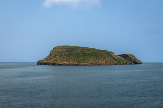 View of Ilh&eacute;u de Cabras from Cruz do Can&aacute;rio viewpoint on Terceira Island, Azores, Portugal, featuring two volcanic islets rising from the Atlantic Ocean under a calm blue sky