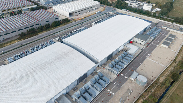 Aerial view of the STACK data center facility featuring large white industrial buildings, numerous rooftop cooling units, and paved access roads in Siziano, Lombardia, Italy.