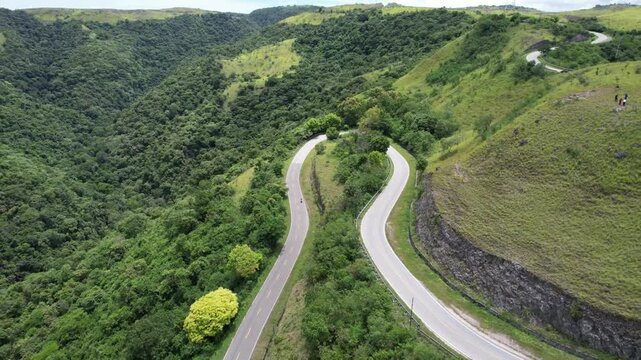 Sweeping landscape of Sumba featuring dramatic hairpin roads, verdant hills, dense forest, and a passing vehicle, showcasing the island&rsquo;s breathtaking tropical terrain.