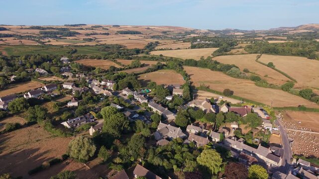 Aerial drone footage of Corfe village in Dorset, England, featuring traditional stone cottages, rolling countryside, green fields, and the scenic Purbeck landscape on a bright summer morning