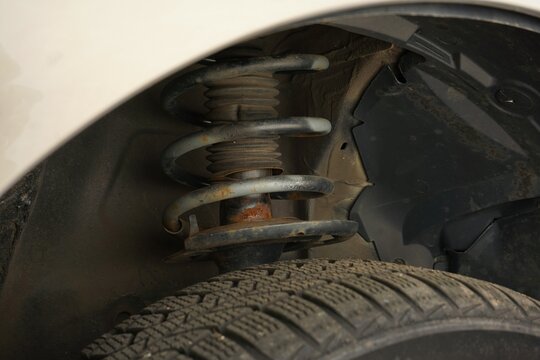 Close-up of a worn suspension strut with rusty coil spring inside a vehicle wheel arch. Concept of automotive repair, suspension inspection, shock absorber replacement and car maintenance.