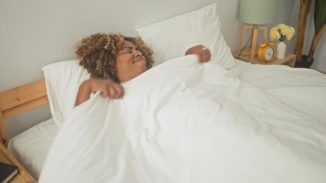 Woman on bed gesturing while tossing a pillow and reaching upward in a bedroom inside a building; restlessness reflection.
