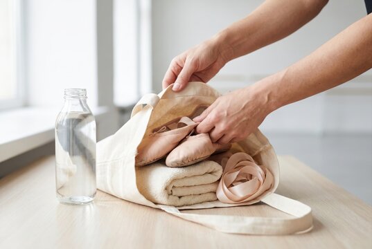 Hands packing ballet pointe shoes ribbons and a towel into a canvas tote bag