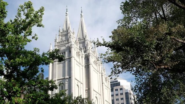 Gothic style architecture of the Mormon Temple in Temple Square, Salt Lake City, UT through the trees that gentle rustle in the breeze.  Wispy clouds gently pass overhead.