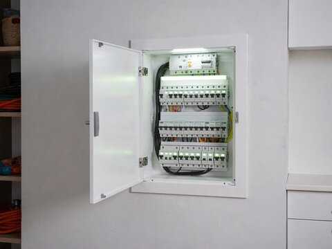 Electrical distribution board with multiple circuit breakers and wiring visible, installed in a modern interior setting with a clean white finish