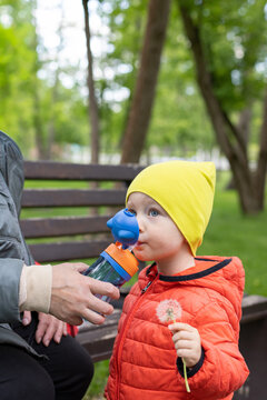 Female hands giving to the little child to drink water from a plastic children bottle.