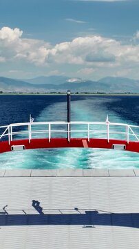 Panoramic vertical view from the ferry deck of the calm sea and mountainous coast, the trail of the ferry against the background of mountains and clouds.