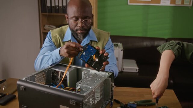 Zoom out shot of African American man and Caucasian young adult woman assembling desktop computer hardware. Perfect for promoting IT support services, hardware repair tutorials, and STEM education