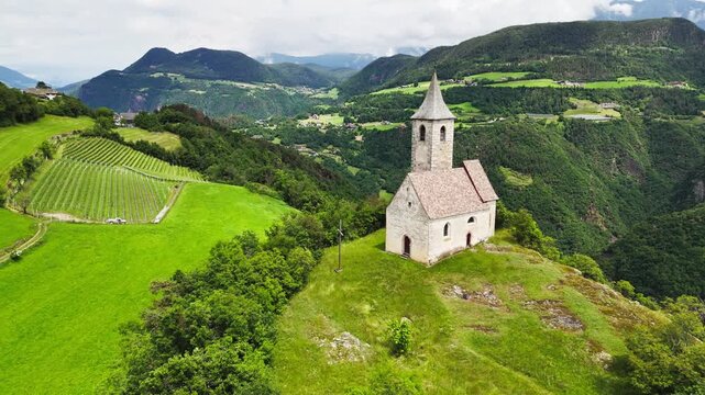 Alpine countryside with hilltop chapel and patchwork fields in South Tyrol, Italy, mountainous Dolomites region, aerial view