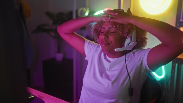 Woman gamer at computer desk wearing headset, hands on head and eyes closed after an intense play in a streaming studio; frustration defeat tension aftermath.