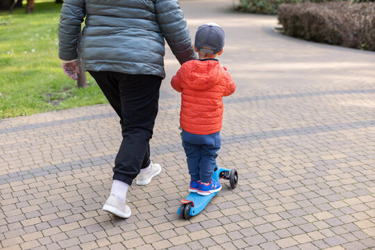  Child riding scooter with grandmother in a public park.